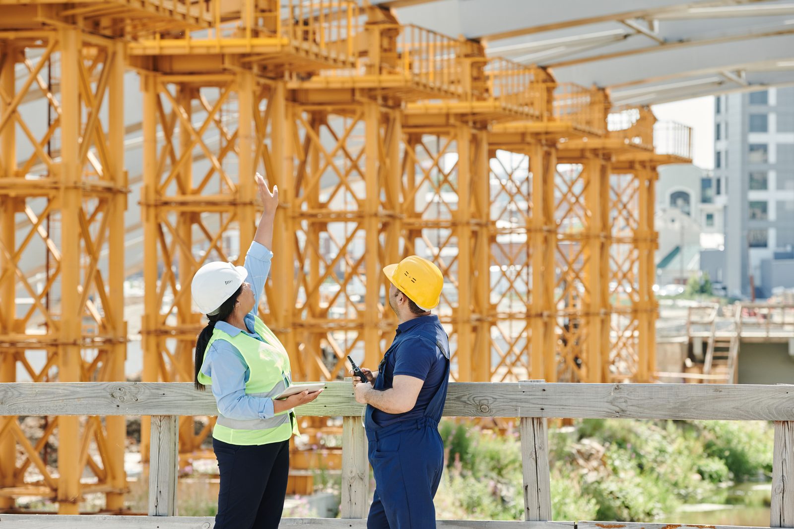 Two site supervisors in hard hats and safety vests discussing work on a construction site