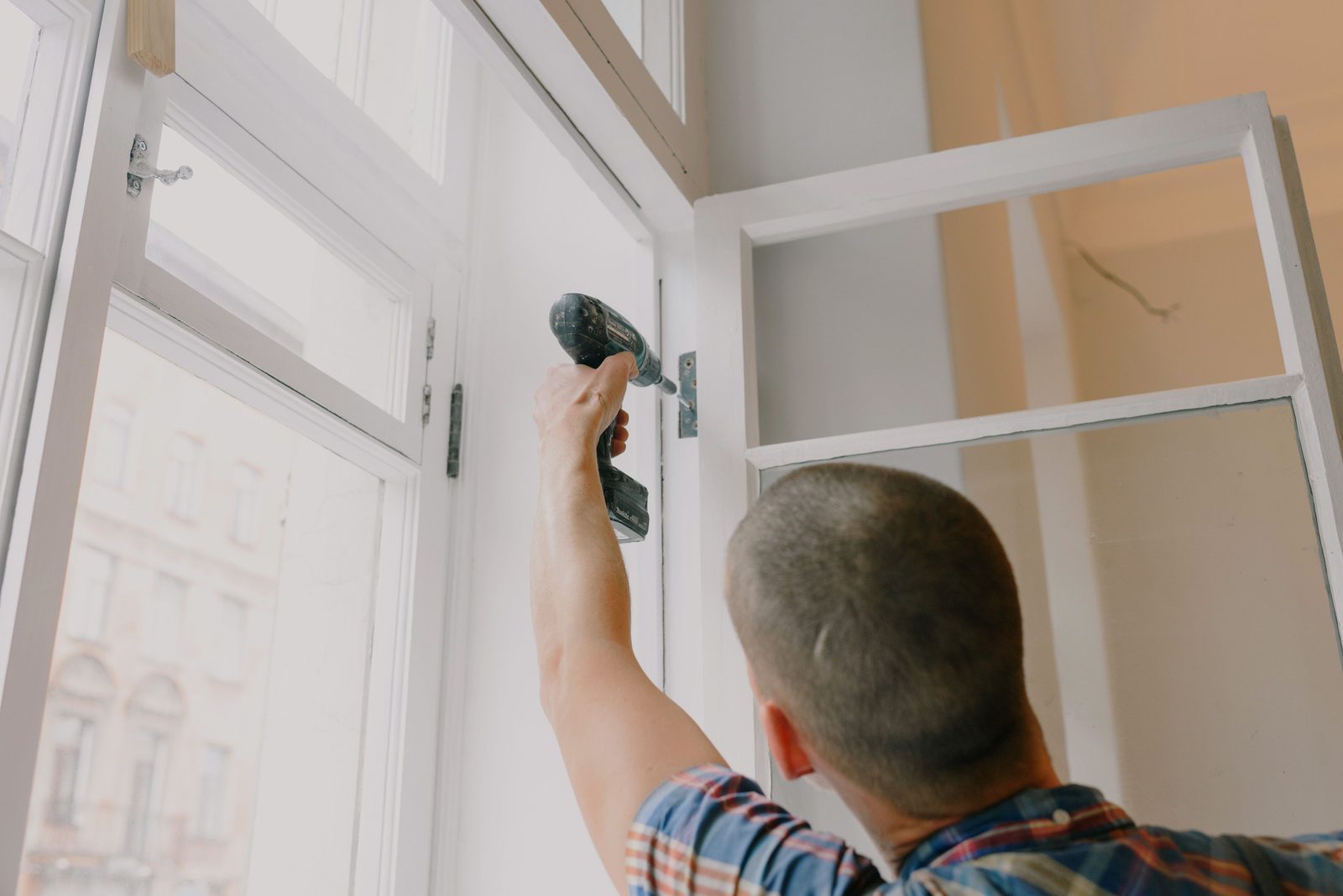 Worker installing a window frame with a power drill