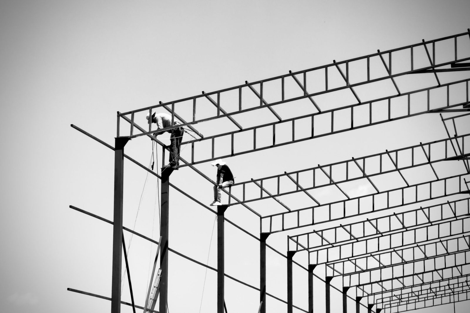 Two ironworkers on a steel framework, bolting structural beams high above the ground